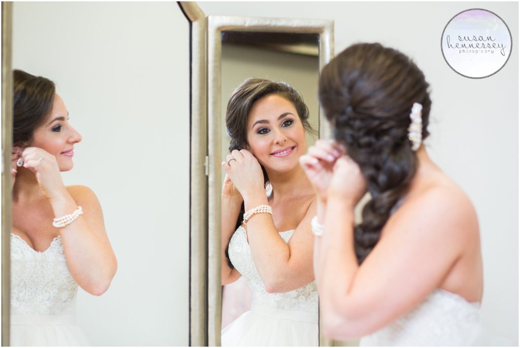 Bride puts on her wedding day earrings in mirror. 