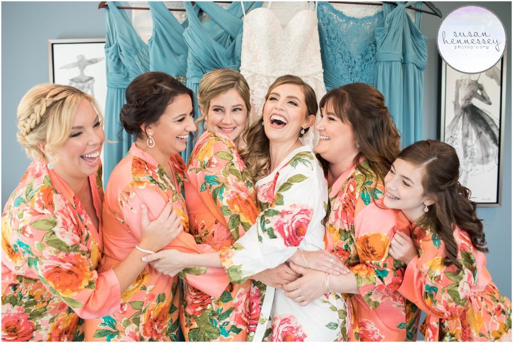 Bride and bridesmaids laugh in matching robes in the bridal suite at the Bradford Estate