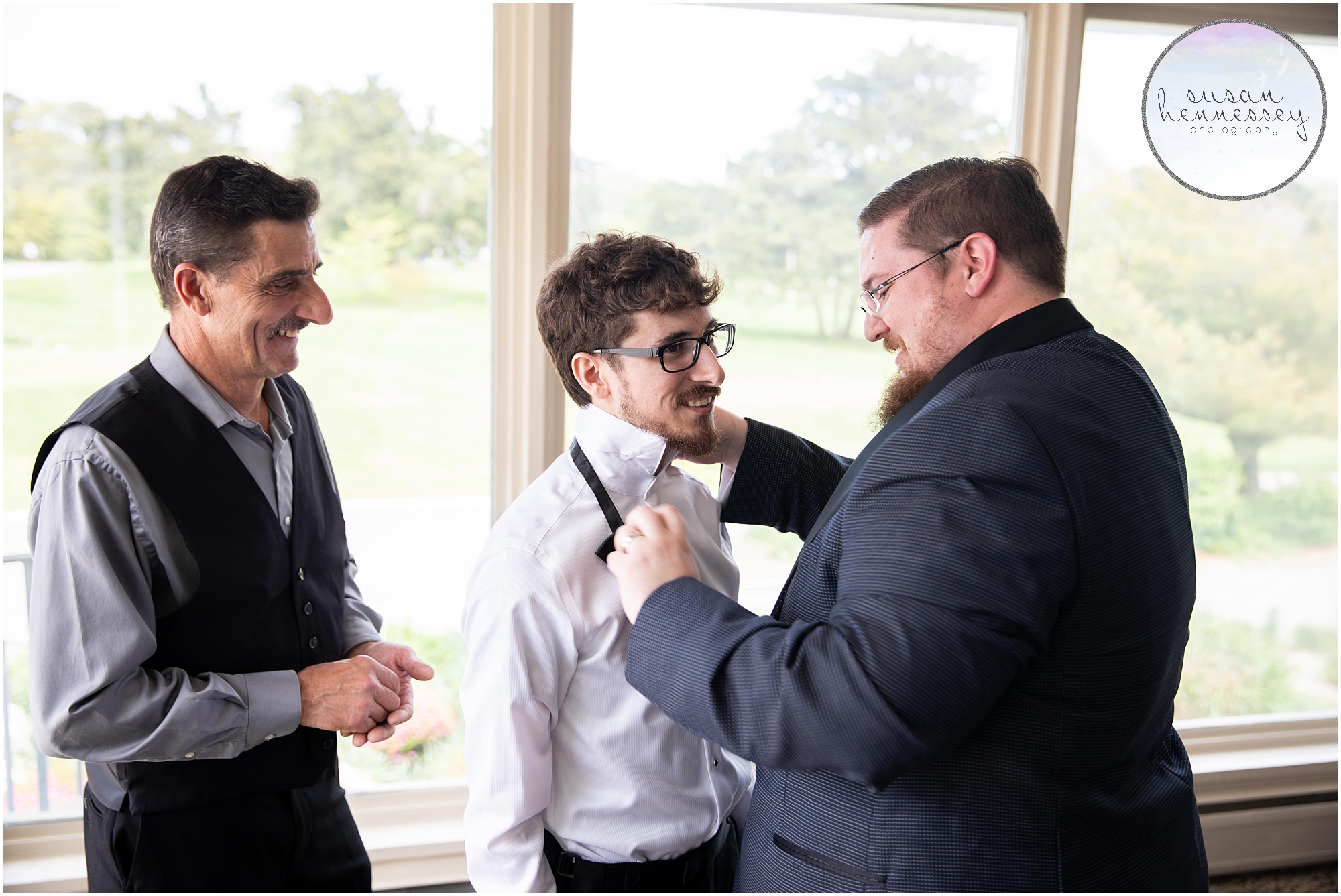 The groom receives help from his father and best man while he gets ready on his wedding day.