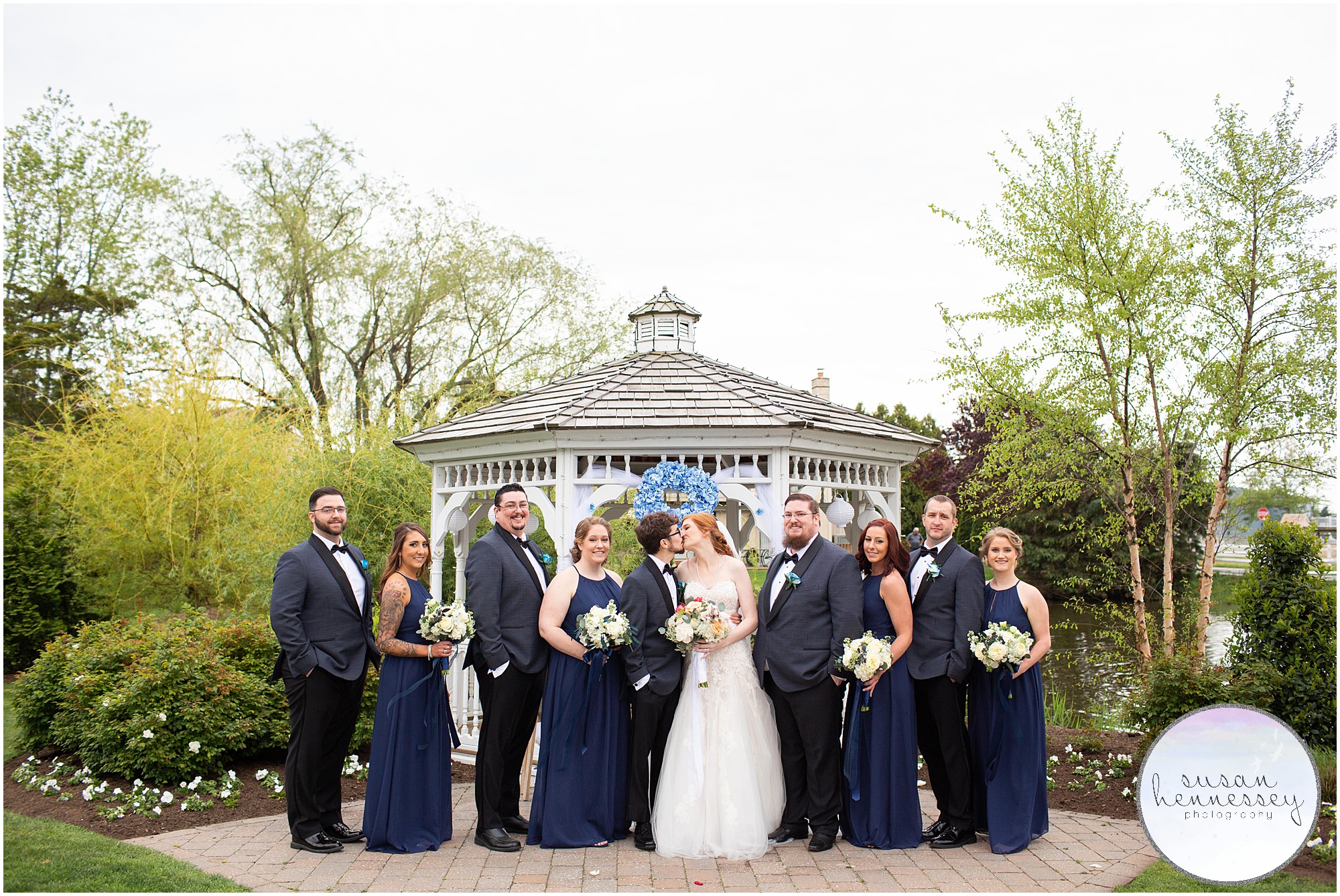 A bride and groom kiss at their wedding with their bridal party.