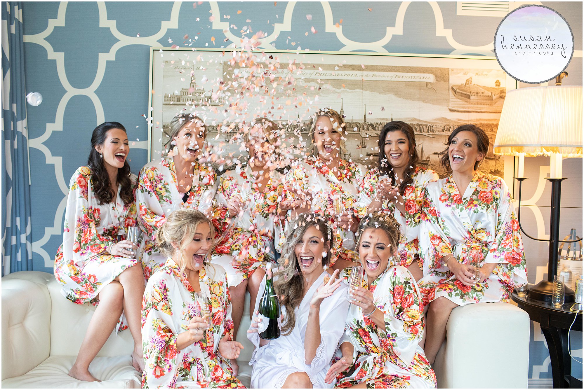 Bride and bridesmaids in floral robes popping champagne and confetti at Hotel Monaco in Philadelphia.