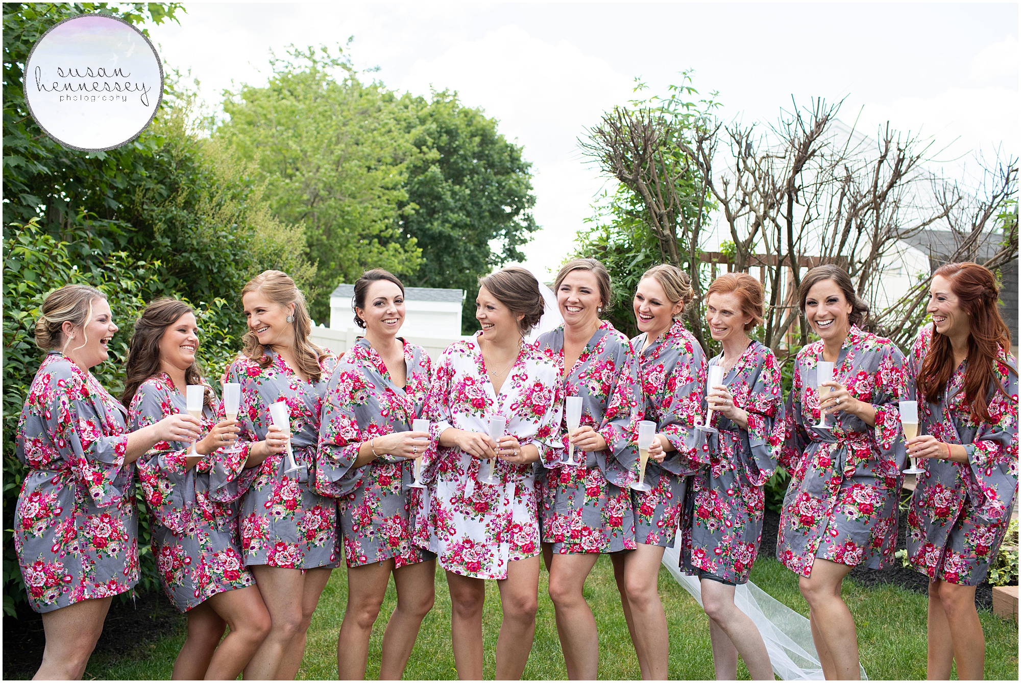 A bride and her bridesmaids in floral robes with champagne.