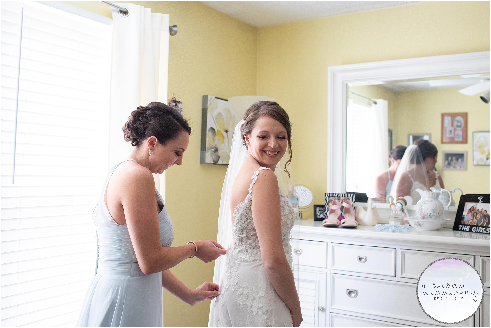 The maid of honor zips the bride into her wedding dress.