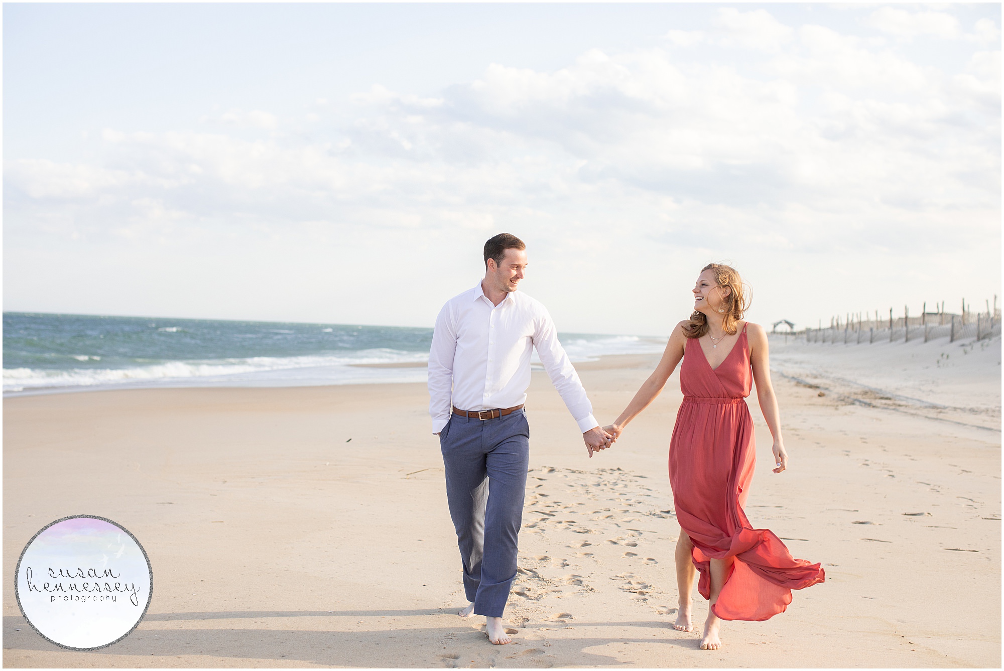 A couple walks on the beach holding hands.