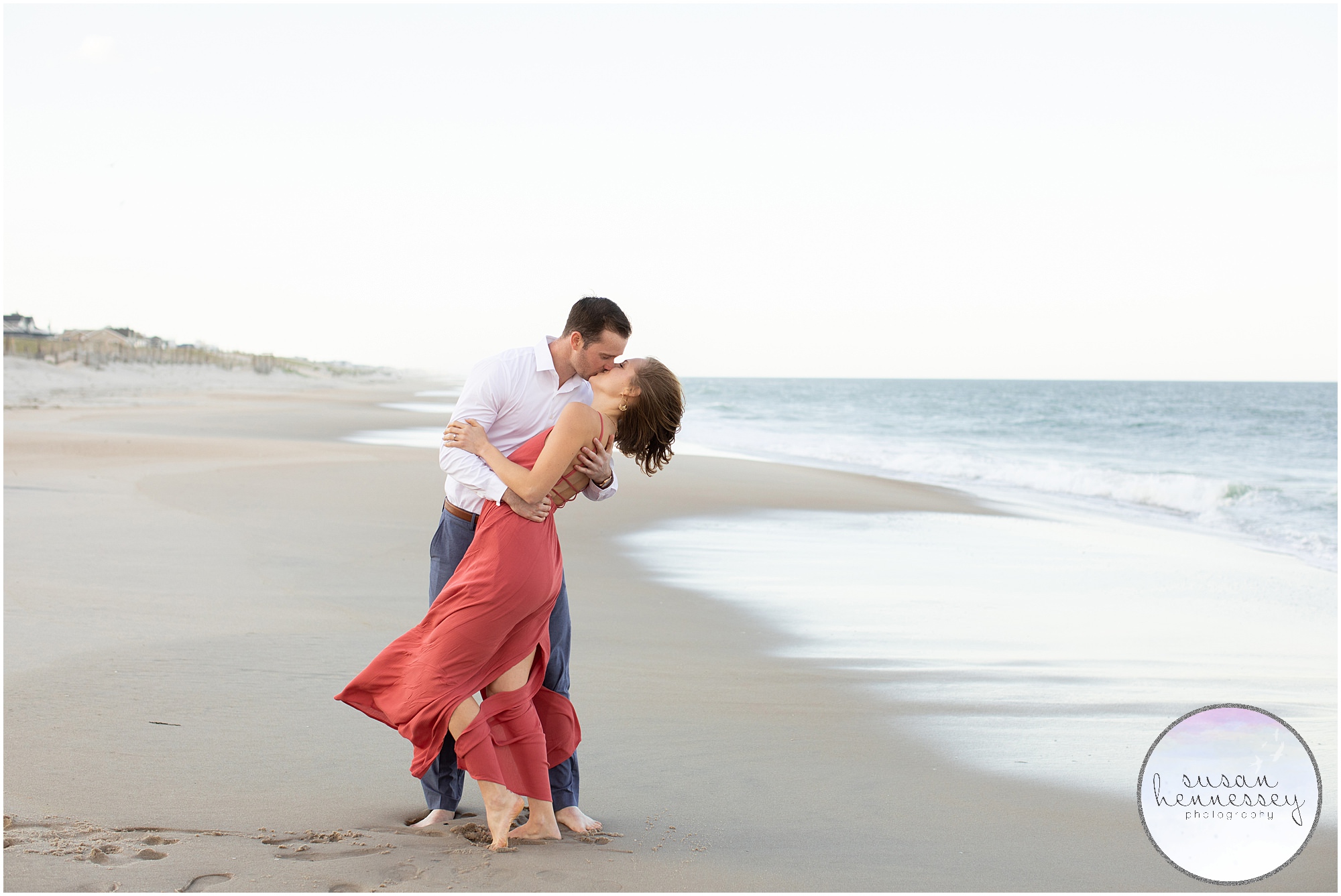 An engaged couple kiss by the ocean.