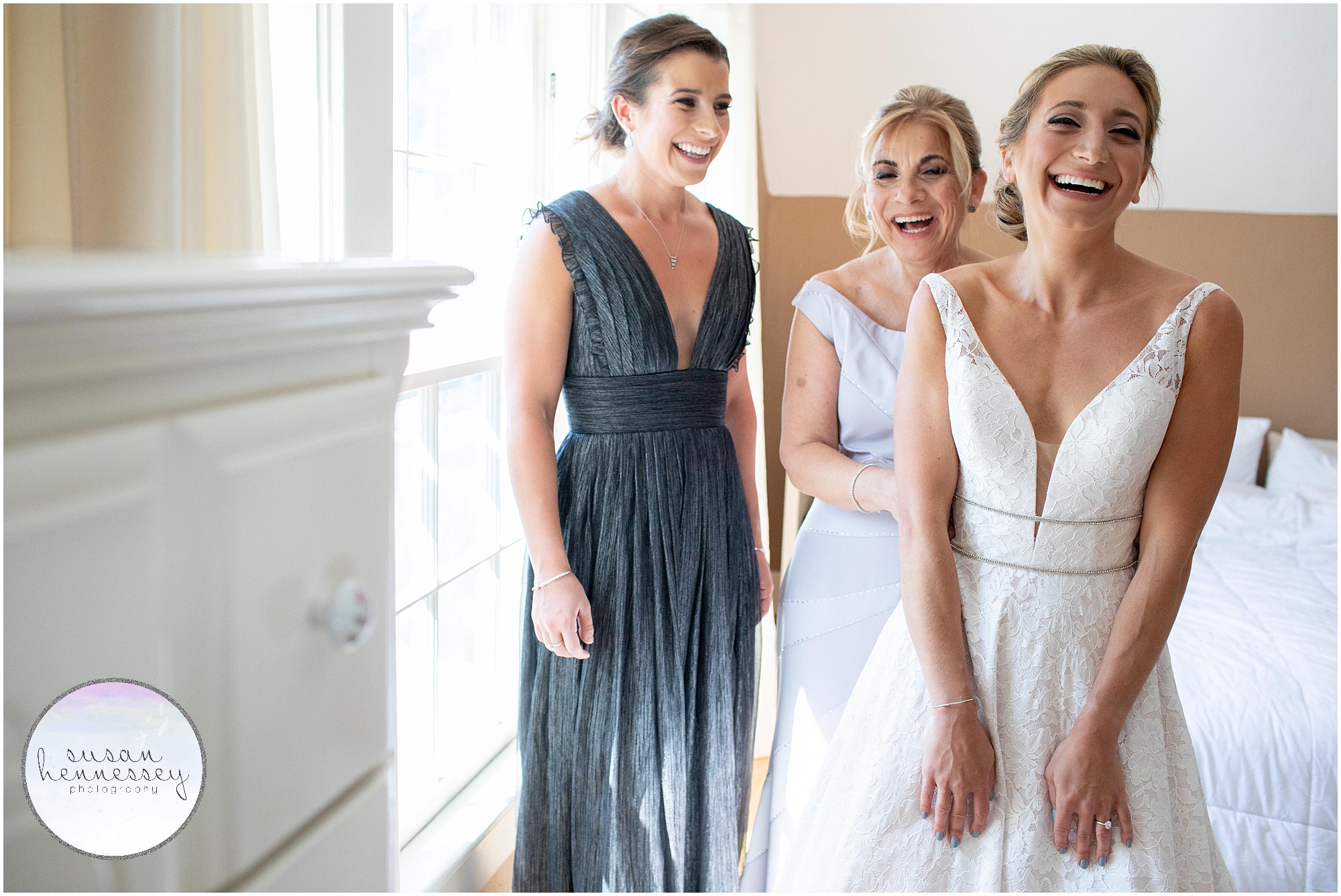 A bride, her mother and sister laugh while she gets zipped into her gown.