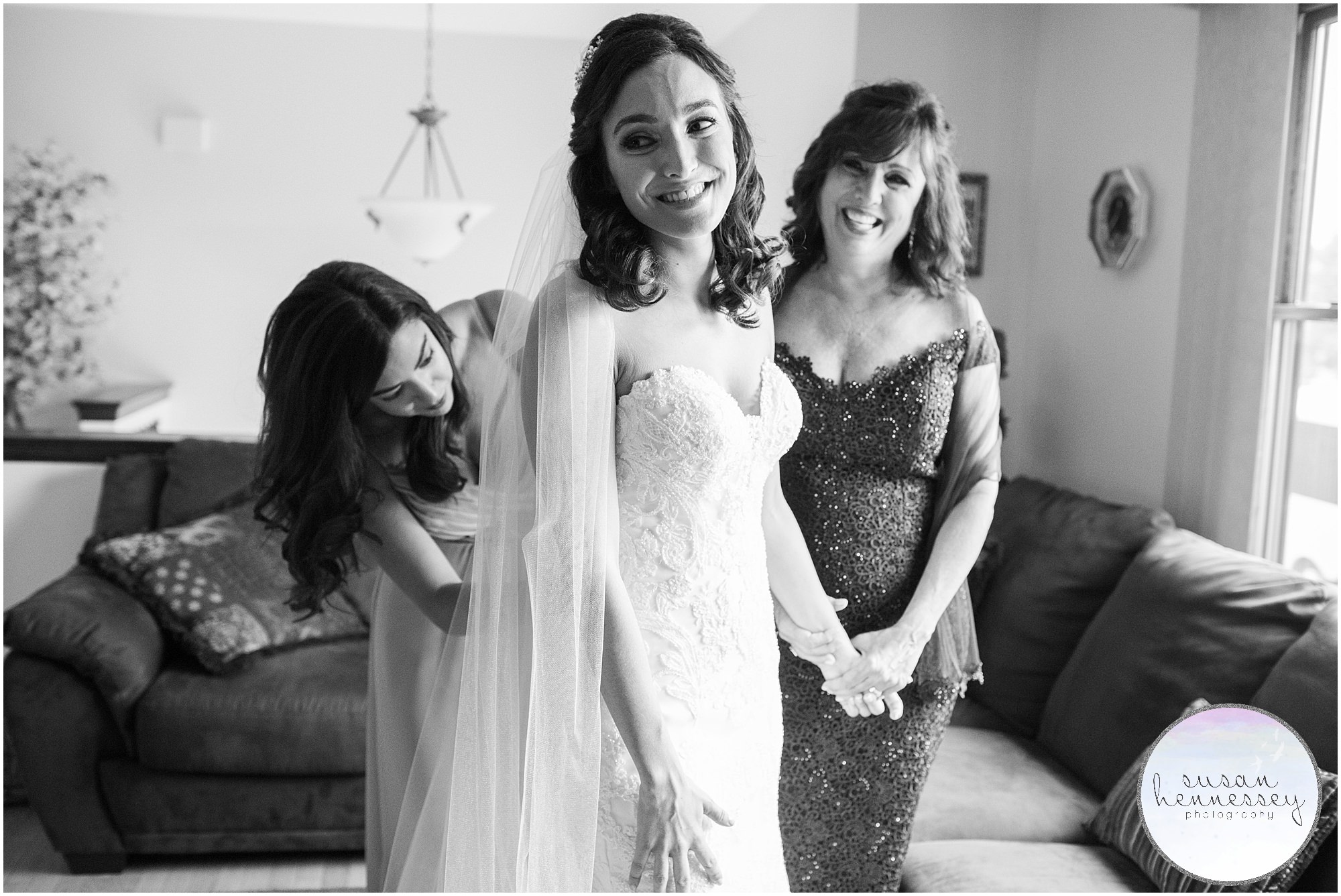 Bride dresses into wedding gown with the help of her maid of honor and mother