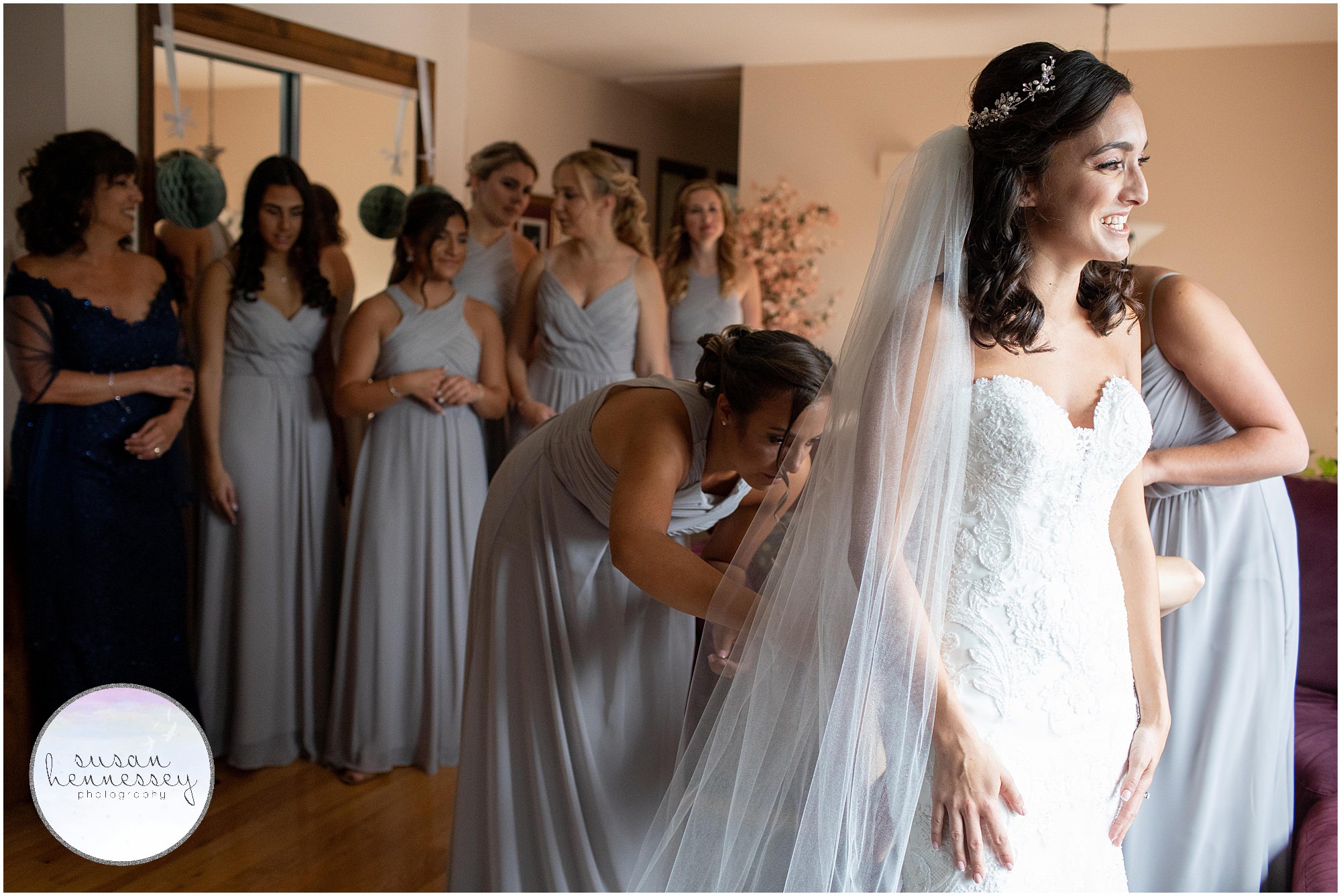 Bridesmaids look on while bride is buttoned into her gown