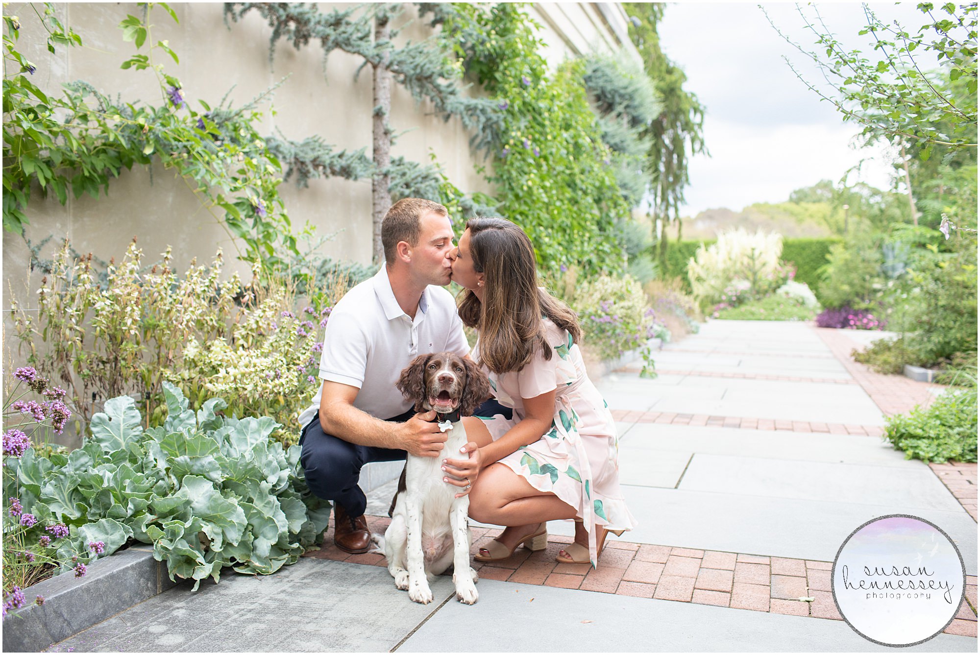 An engaged couple kiss while photographed with their dog.