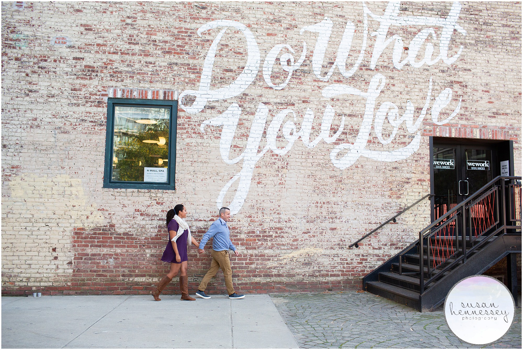 An engaged couple walk along the "Do What You Love" mural in Philadelphia