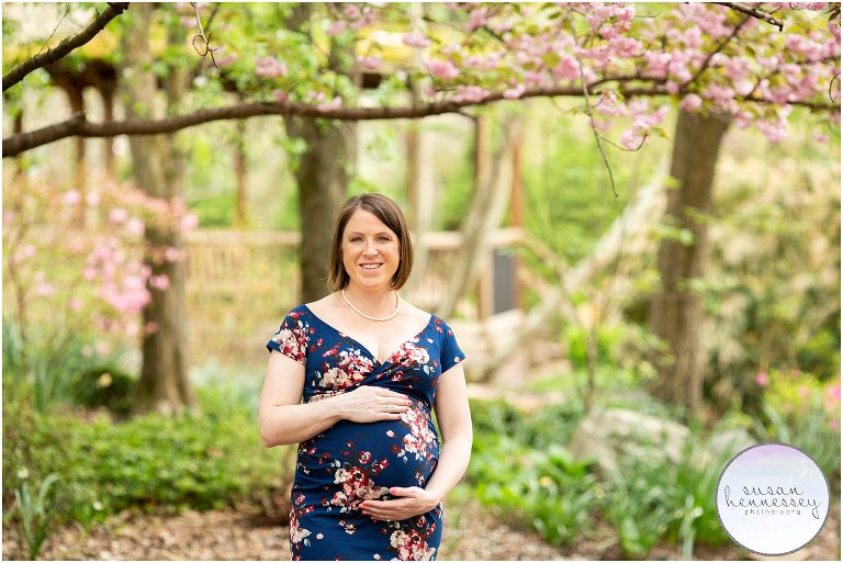 A glowing mother to be wearing a blue floral maternity gown at her Cherry blossom maternity session