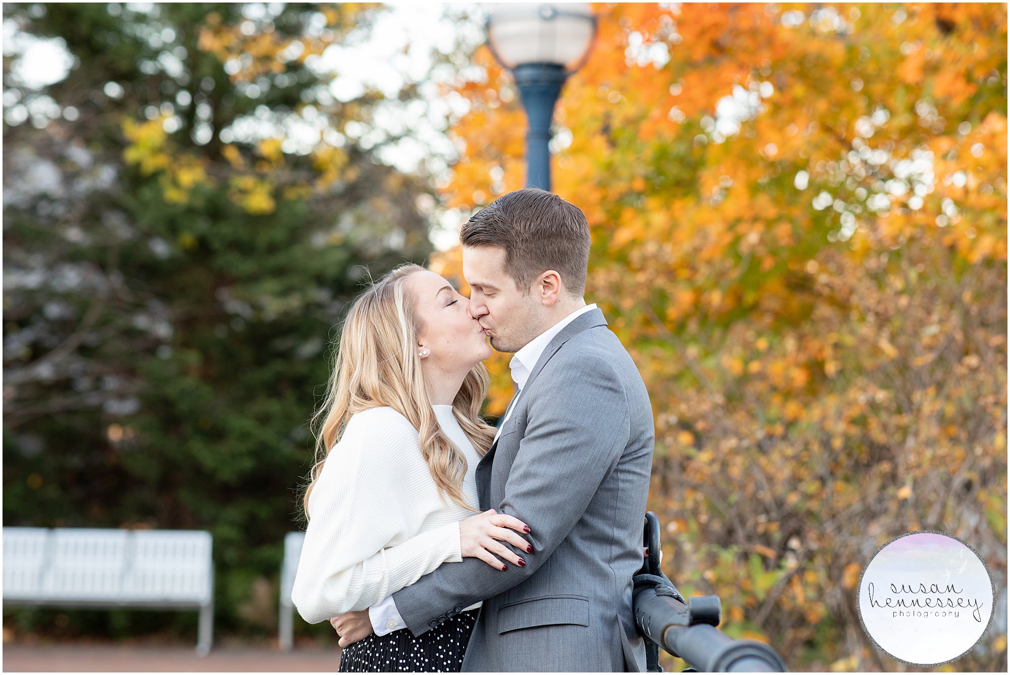 A couple kiss at their downtown Frederick engagement session on the bridge with fall foliage. 