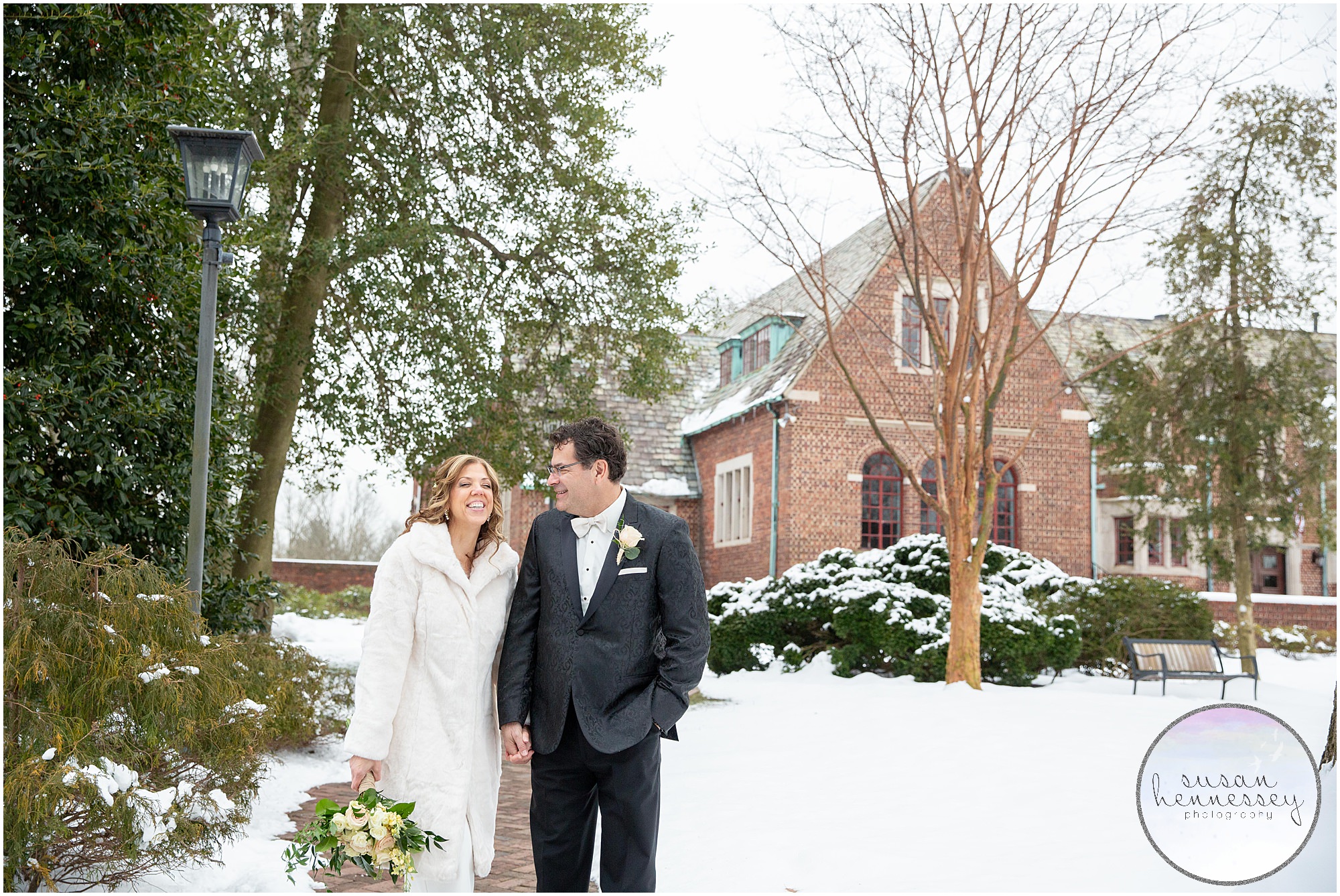 A couple walk hand in hand at their winter microwedding with the community house of moorestown in the background