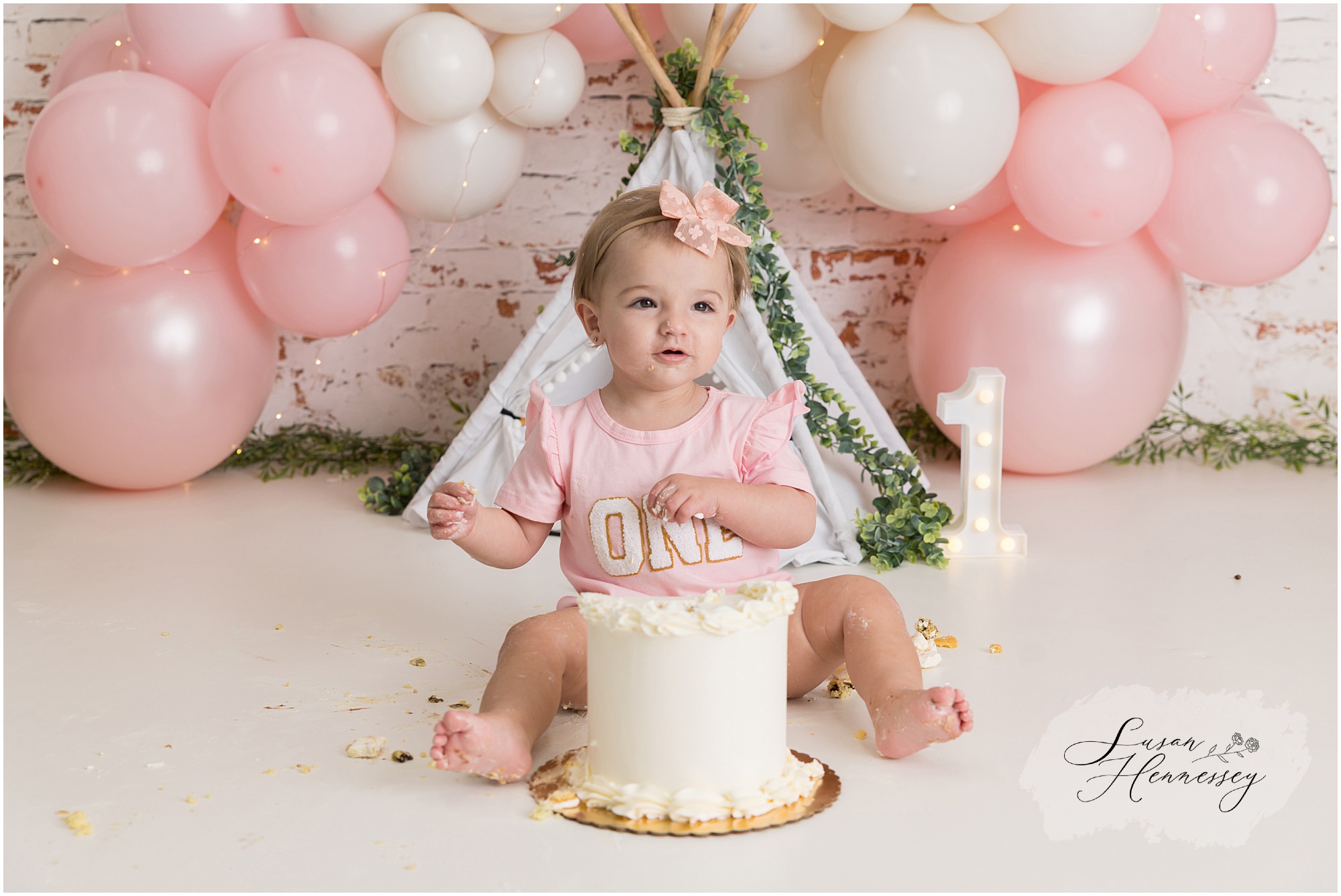 Baby girl sitting in front of pink and white balloon arch during her South Jersey cake smash photography session